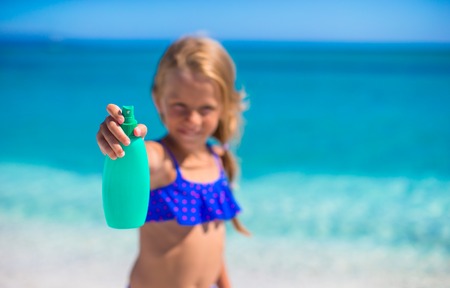 Little adorable girl in swimsuit with suntan lotion bottleの写真素材