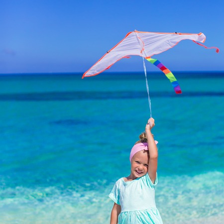 Little happy girl playing with flying kite on tropical beachの写真素材