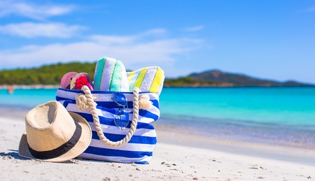 Blue bag, straw hat, flip flops and towel on white beachの写真素材