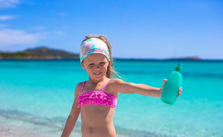 Little adorable girl in swimsuit with suntan lotion bottleの写真素材
