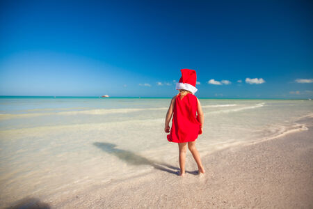 Little adorable girl in red Santa hat at tropical beachの写真素材