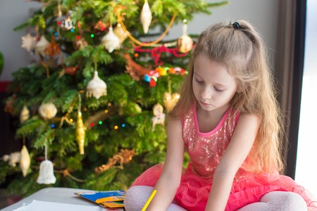 Adorable little girl drawing near Christmas treeの写真素材