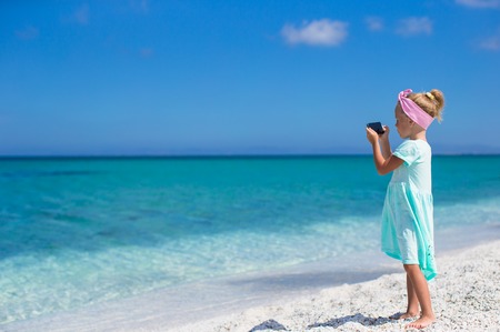 Little cute girl taking pictures on phone at tropical beachの写真素材