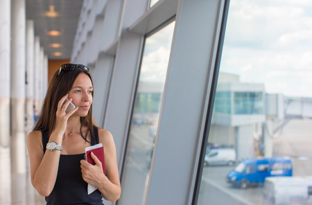 Woman talking by cell phone with boarding passport at airportの写真素材