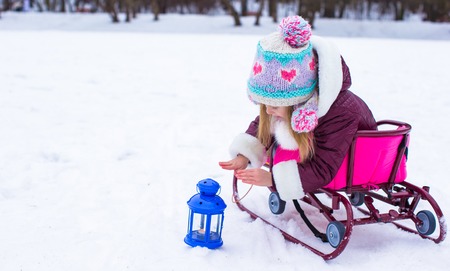 Little girl warms her hands on candle in the lantern outdoorsの写真素材