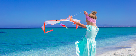 Little happy girl playing with flying kite on tropical beachの写真素材