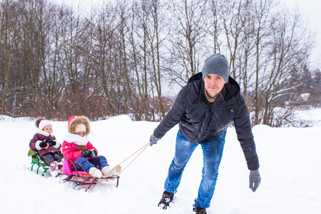 Young father with little daughters sledding in winter outdoorsの写真素材