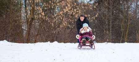Little girl and happy father sledding in winter snowy dayの写真素材