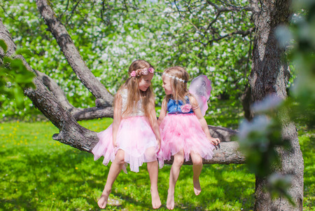 Little adorable girls sitting on blossoming tree in apple gardenの写真素材