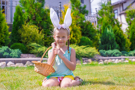 Adorable little girl wearing bunny ears holding basket with Easter eggsの写真素材
