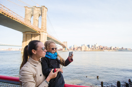 Mother and adorable little daughter taking selfie on background of Brooklyn Bridgeの写真素材