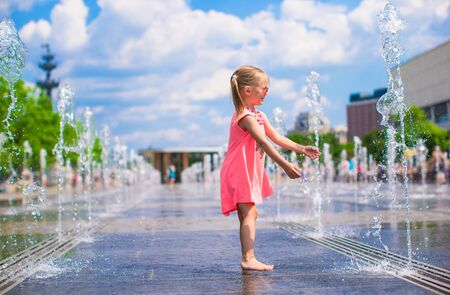 Little girl playing in open street fountain at hot sunny dayの写真素材