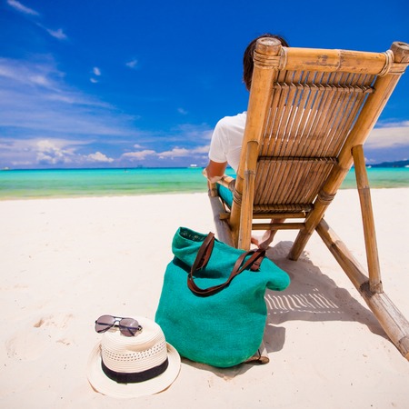 Young man relaxing in wooden chair on white sand beach