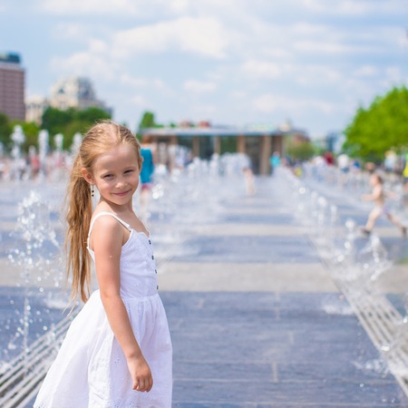 Little happy girl have fun in street fountain at hot sunny dayの写真素材