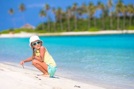 Adorable little girl drawing picture on white beachの写真素材