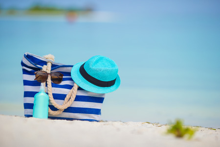 Blue bag, straw hat, sunglasses and sunscreen bottle on white beachの写真素材