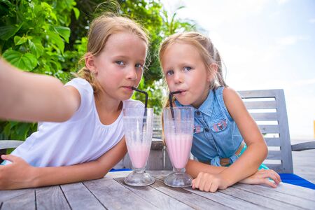 Little girls taking selfie and drinking tasty cocktails at tropical resortの写真素材