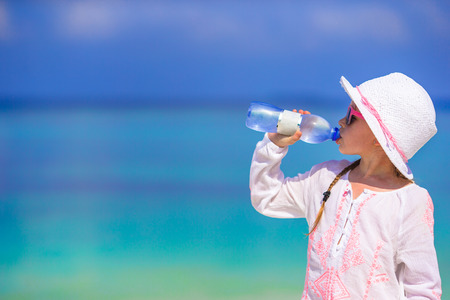Little girl drinking mineral bottle of water at hot summer day on beachの写真素材