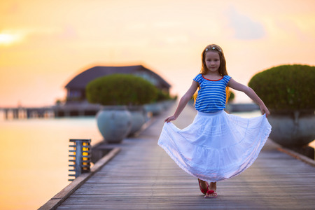 Silhouette of adorable little girl on wooden jetty at sunsetの写真素材