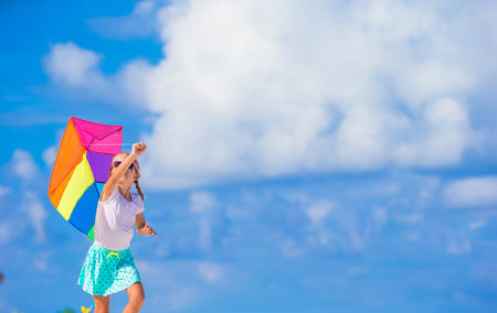 Little happy girl playing with flying kite on tropical beachの写真素材
