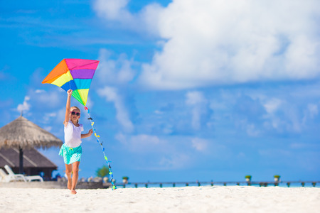 Little happy girl playing with flying kite on tropical beachの写真素材