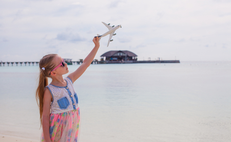 Happy little girl with toy airplane in hands on white sandy beachの写真素材