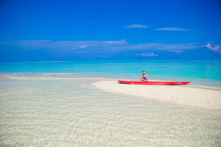 Little girl in yoga position on surfboard at tropical beachの写真素材