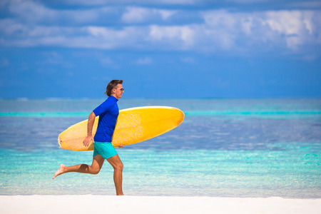 Happy young surf man runing at the beach with a surfboardの写真素材