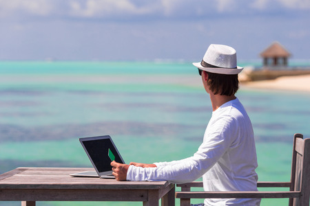 Young man working on laptop with credit card at tropical beachの写真素材