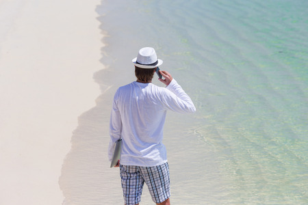 Young man talking by cell phone on tropical beachの写真素材