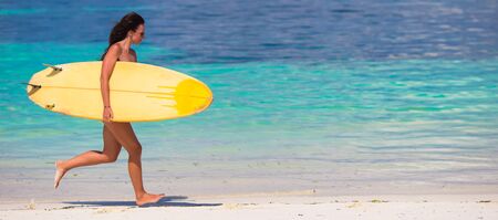 Happy young surf woman runing at the beach with a surfboardの写真素材