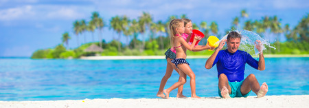 Adorable little girls having fun with dad on white beachの写真素材