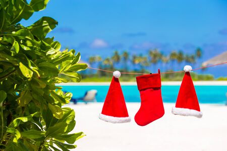 Red Santa hats and Christmas stocking hanging on tropical beachの写真素材