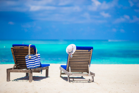 Lounge chairs with bag and hat on tropical white beachの写真素材