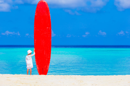 Adorable little girl with big surfboard during tropical vacation