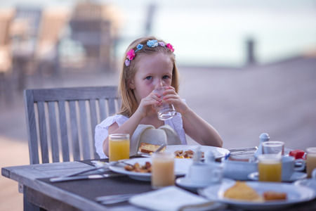 Adorable little girl having breakfast at outdoor cafeの写真素材