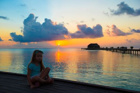 Silhouette of adorable little girl on wooden jetty at sunsetの写真素材