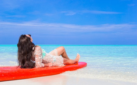 Happy beautiful surfer woman at white beach on red surfboard