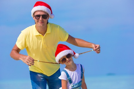 Little girl and happy dad in Santa Hats enjoy beach vacationの写真素材