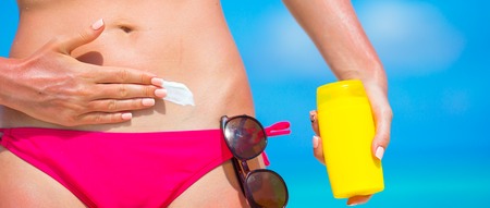 Closeup female hand applying with sunscreen on white beach