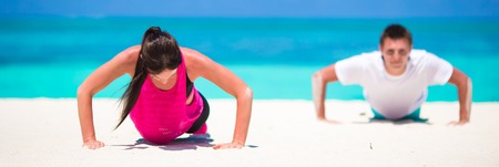 Young fitness couple doing push-ups during outdoor cross training workout on tropical beach