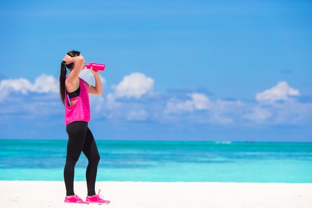 Fit young woman drink water on white beachの写真素材