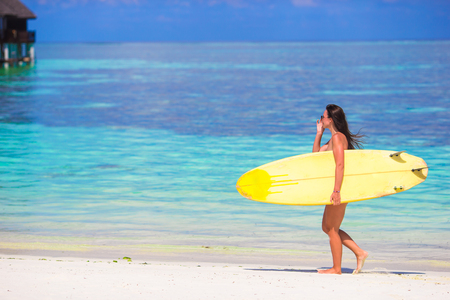 Happy shapely surf woman at white beach with yellow surfboardの写真素材