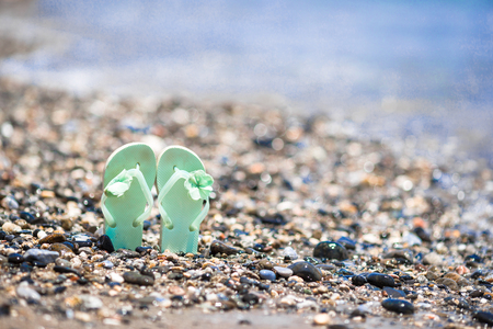 Kids flip flops on beach in front of the blue seaの写真素材