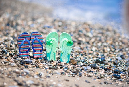 Kids flip flops on beach in front of the blue seaの写真素材