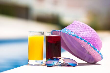 Sunglasses, orange juice, and straw white hat on summer vacation near poolの写真素材