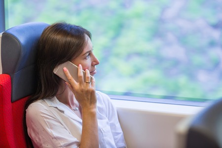 Young business woman talking on the phone traveling by trainの写真素材