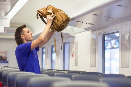 Young man putting luggage on the top shelf at aircraftの写真素材