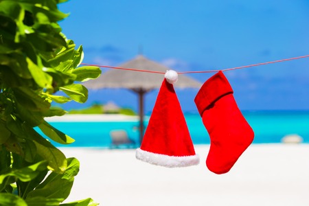 Red Santa hat and Christmas stocking hanging on tropical beachの写真素材