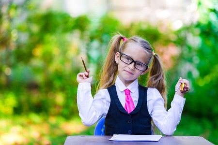 Happy little schoolgirl with notes and pencils going back to school outdoor